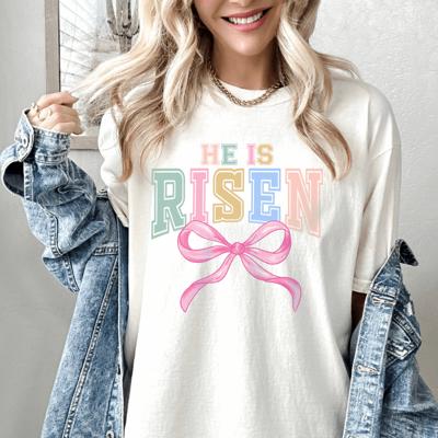 He Is Risen Pastel Varsity Tee with Pink Bow, Preppy Easter Shirt, Colorful Christian Spring Graphic Tee, Women’s Easter Outfit